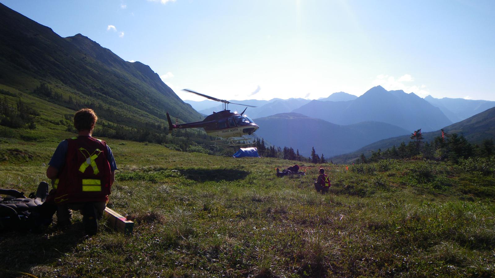 Exploration crew drop off in mountain valley with helicopter in background
