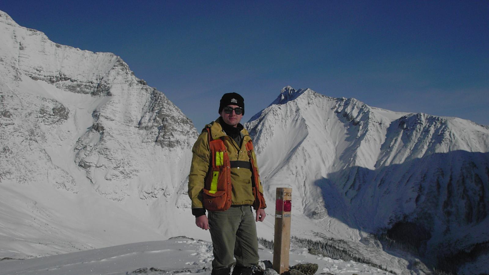 A geologist posing with mineral claim post in a snowy mountain landscape 