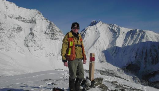 A Man standing at a Claim Post with snow covered mountains in the background