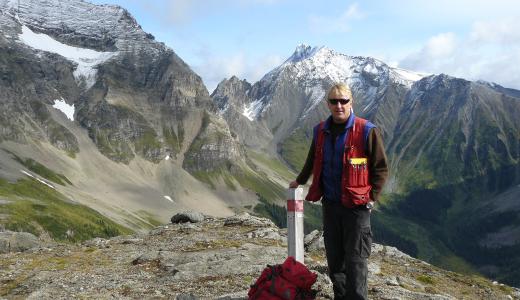 A man standing at a claim post with mountains in the background