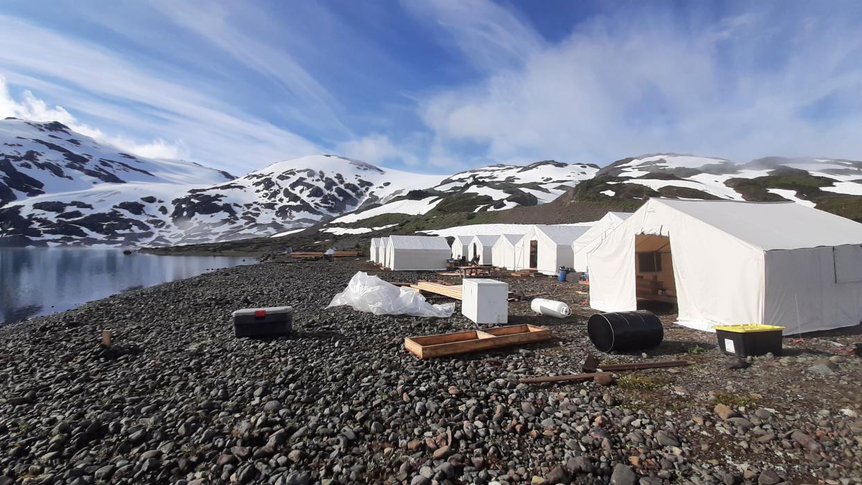 Exploration camp of wall tents with lake and snowy mountains in background