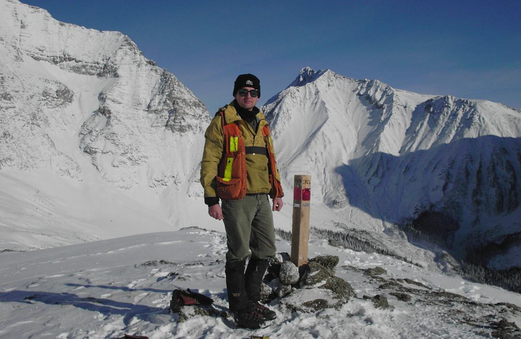 A Man standing at a Claim Post with snow covered mountains in the background