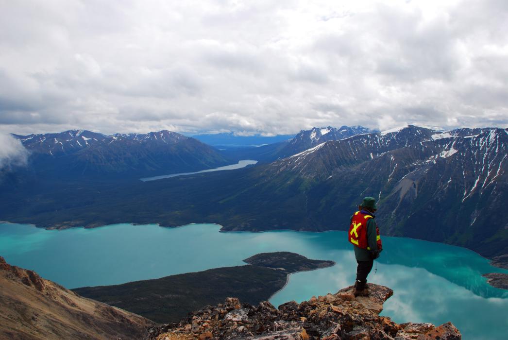 A geologist on mountain ledge overlooking a large lake in Northwwest BC