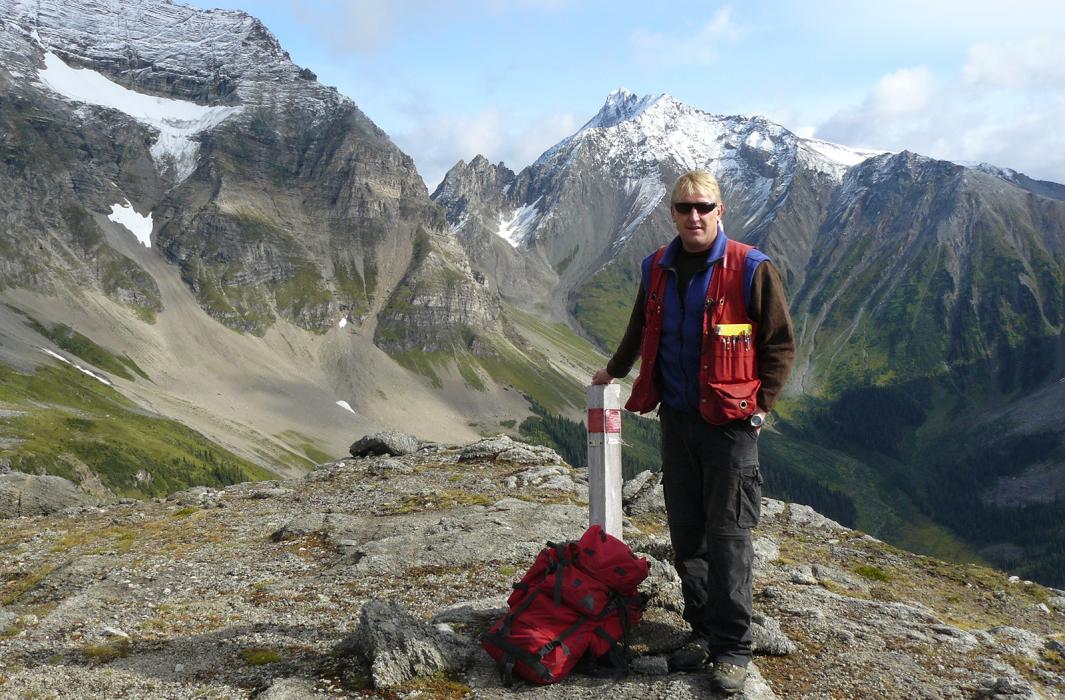 A man standing at a claim post with mountains in the background